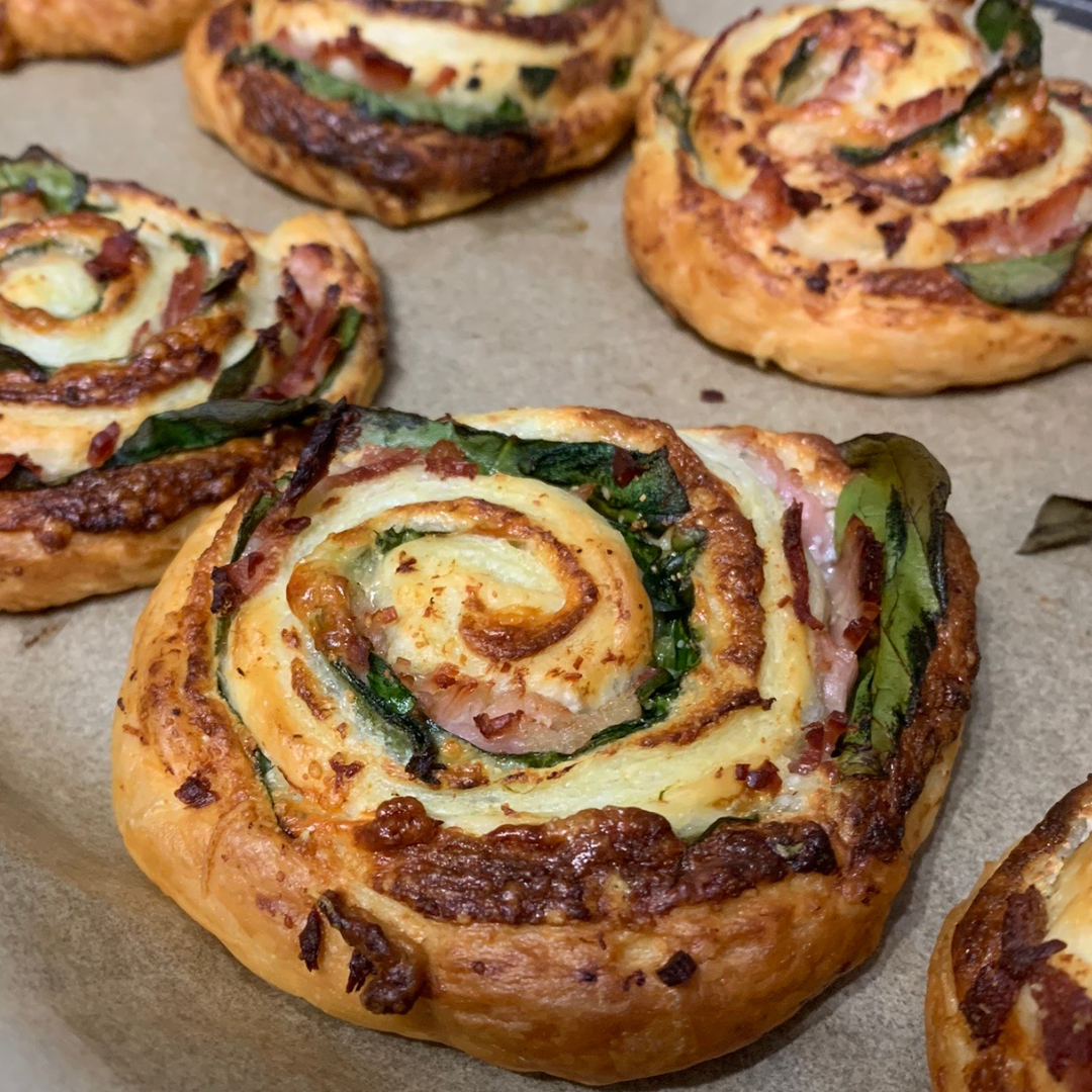Golden-baked pizza pinwheels with spinach, ham, and cheese on a baking tray.
