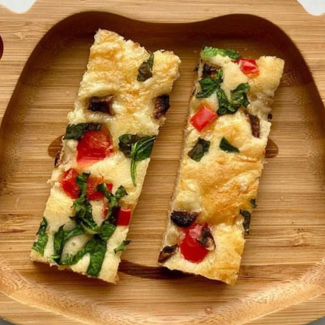 Two golden savoury sheet pancakes with spinach, tomato, and mushrooms on a wooden plate.