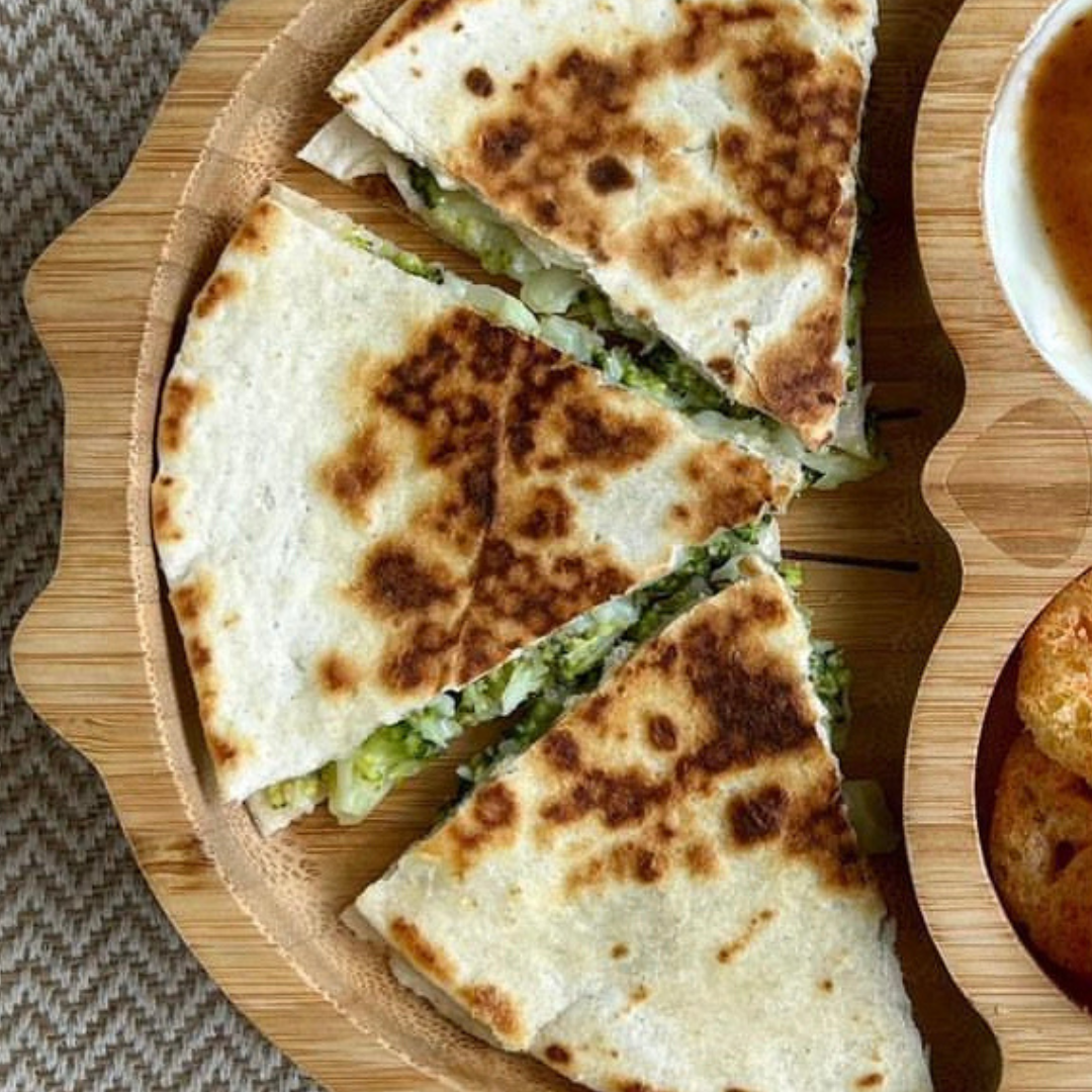 Golden-brown broccoli cheese quesadilla wedges on a wooden plate.