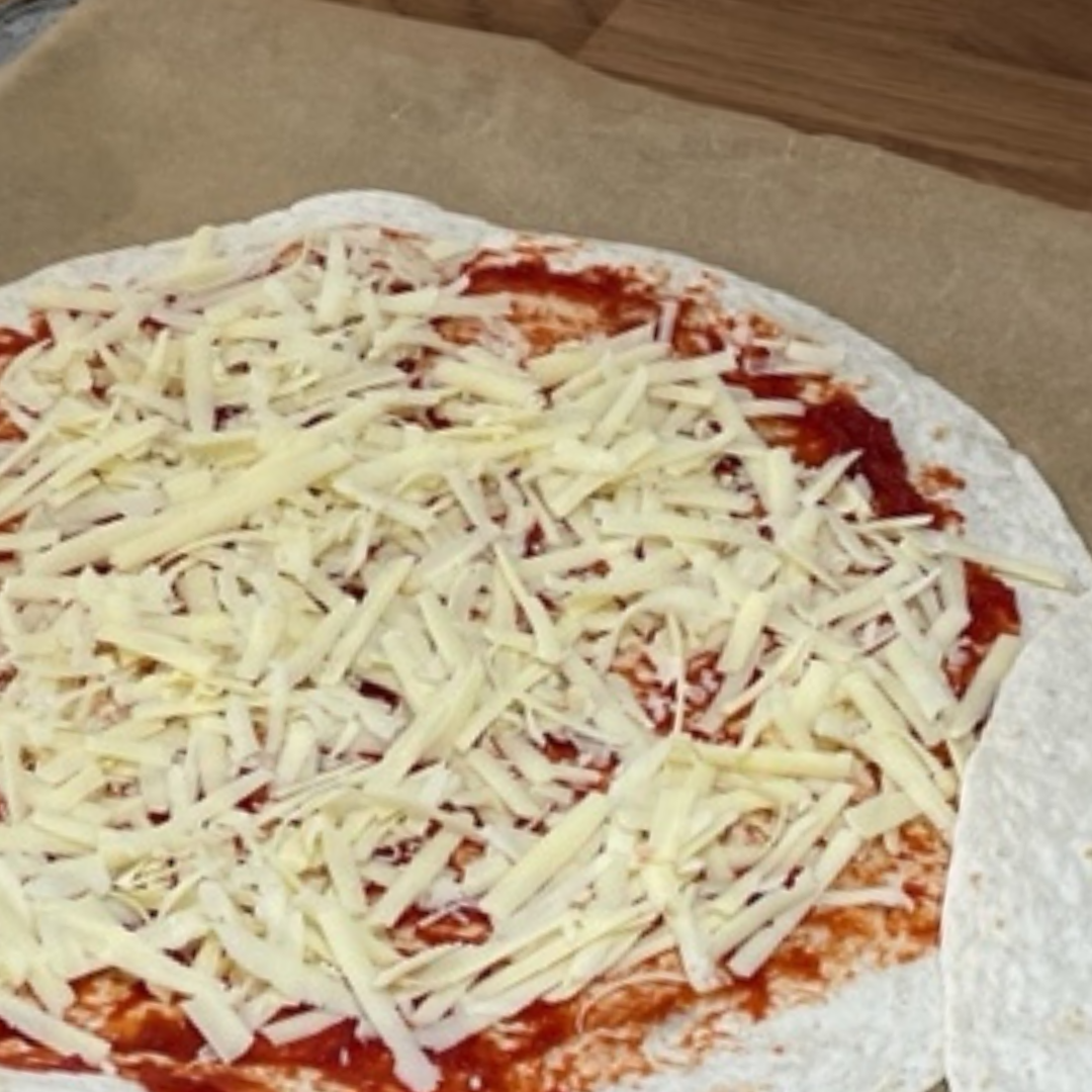 A tortilla wrap pizza base with tomato sauce and a generous layer of grated cheese.