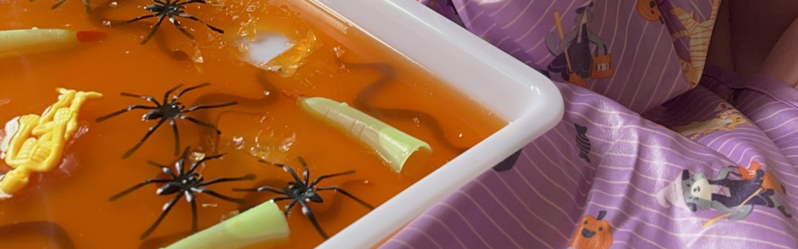 Orange jelly sensory play with plastic spiders, snakes, and green sweets in a white tray.