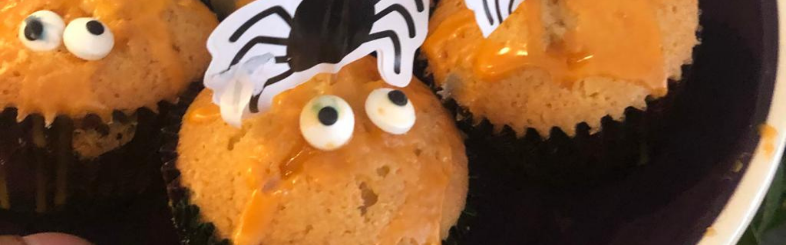 Halloween cupcakes with orange icing, googly eyes, and a spider decoration.