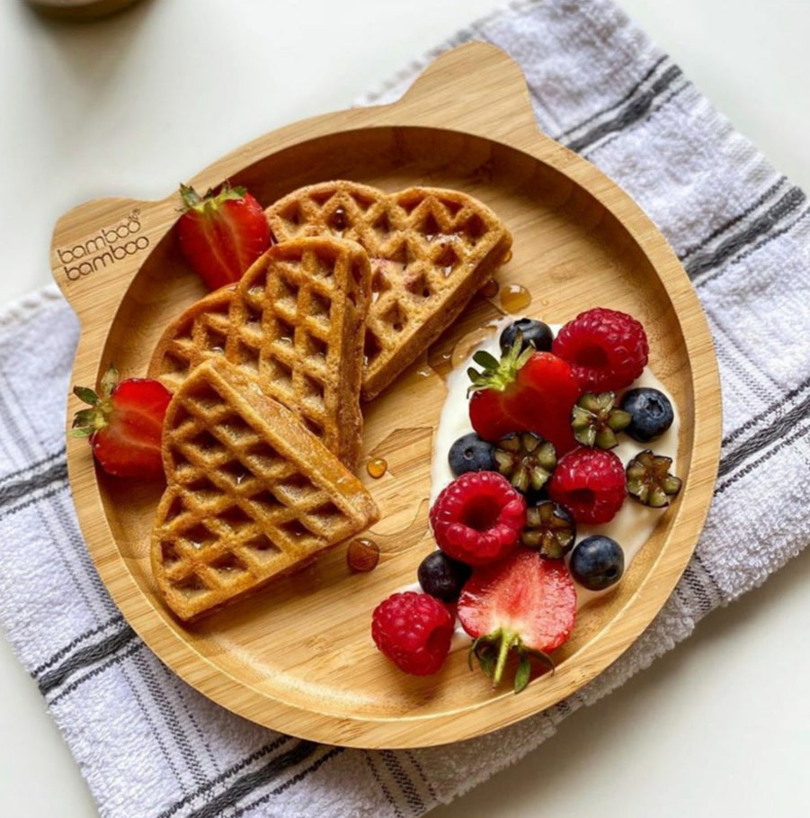 Heart-shaped waffles with strawberries, raspberries, blueberries, and yoghurt on a bamboo plate.