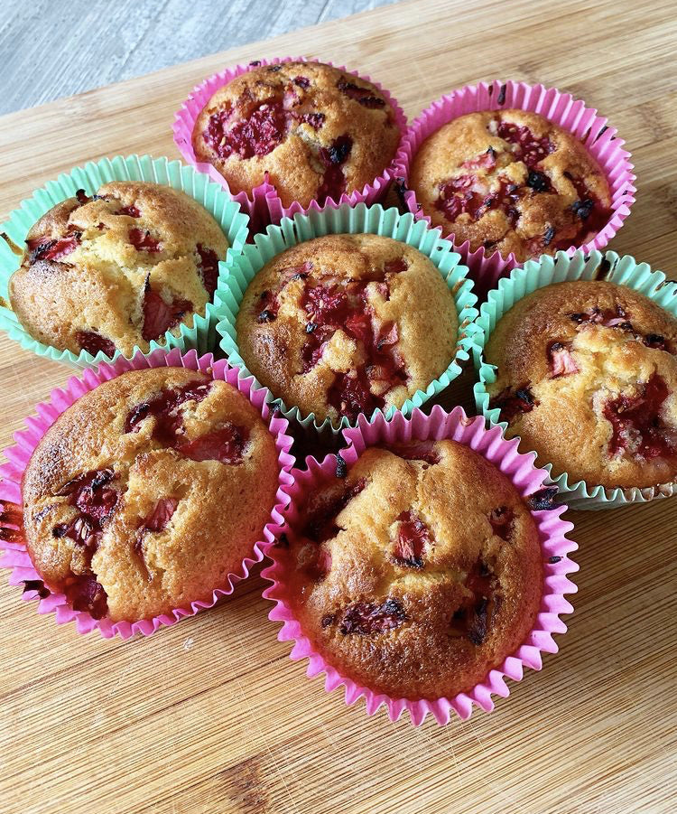 Freshly baked strawberry muffins in colourful pink and mint green paper cases on a wooden board.