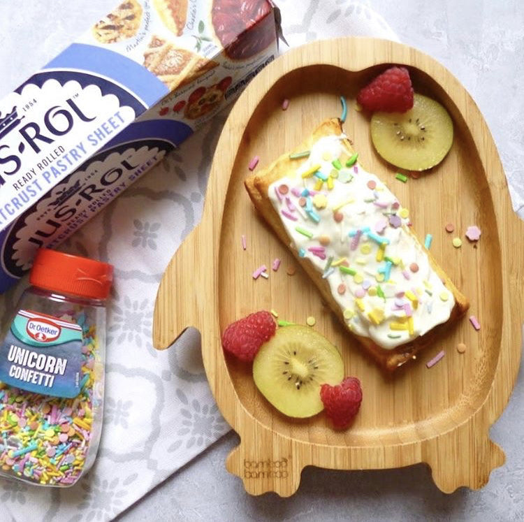 Homemade Pop Tart with white icing and colourful sprinkles on a bamboo plate with raspberries and kiwi.