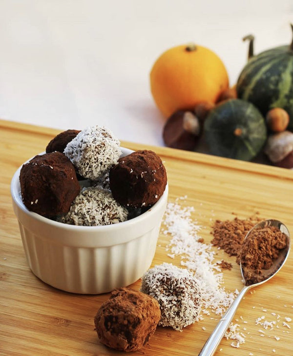 Avocado and almond truffles, some coated in cocoa, others in coconut, on a wooden board.