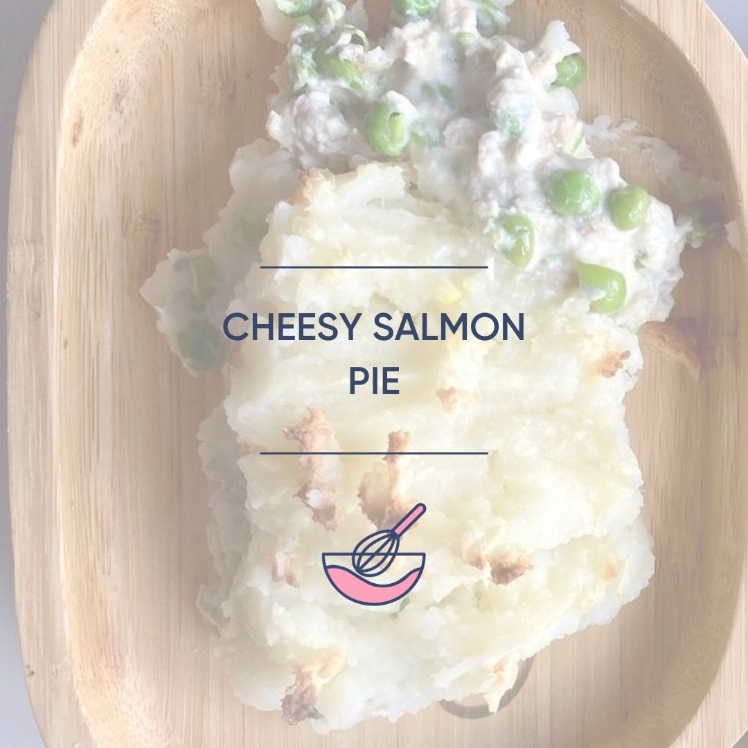 Golden-brown cheesy salmon pie with mashed potato topping and green peas on a wooden plate.