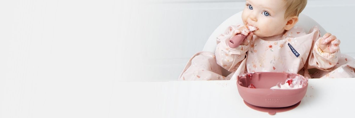 Baby in a pink floral bib chewing a teether, representing weaning essentials.