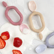 Two Dippit™ multi-stage baby spoons in pink and beige, with textured dippers and easy-grip handles, on spilled yogurt with strawberries.