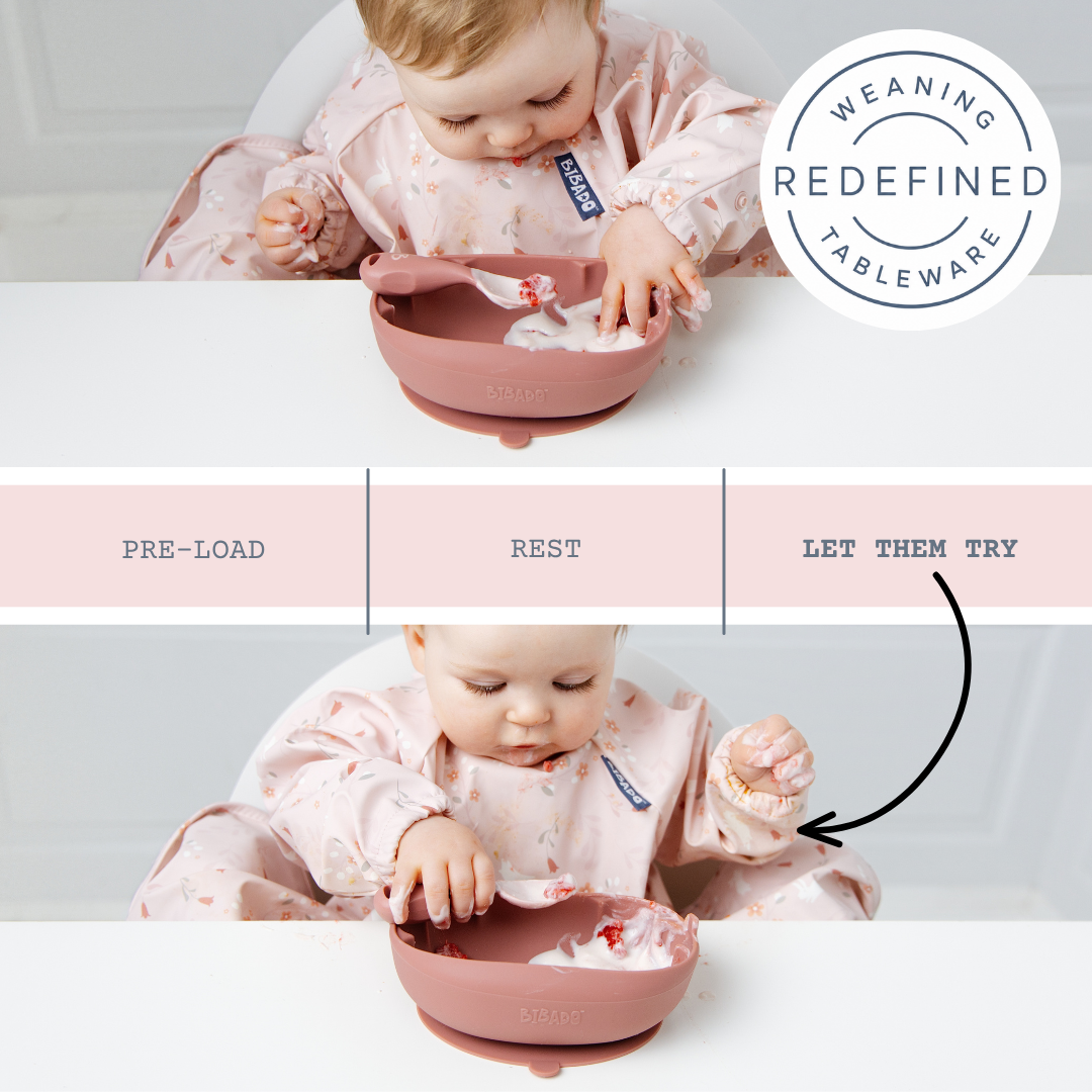 A baby in a pink patterned bib sits in a high chair using a dusty rose silicone suction bowl and spoon. The image is a collage showing three stages: pre-load, rest, and let them try, with a circular badge reading 'Weaning Redefined Tableware'. - Product image