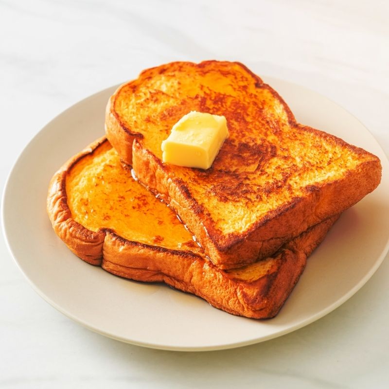 Golden French toast slices with a pat of butter on a white plate.