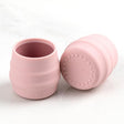 Two small, light pink silicone Sippit™ open training cups, one upright, one on its side revealing a textured base.