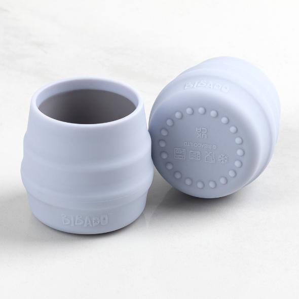 Two light blue Bibado Sippit silicone open training cups, one upright, one on its side showing the textured base. - Product image