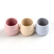 Three small, ribbed silicone Sippit™ open training cups in pink, cream, and light blue.