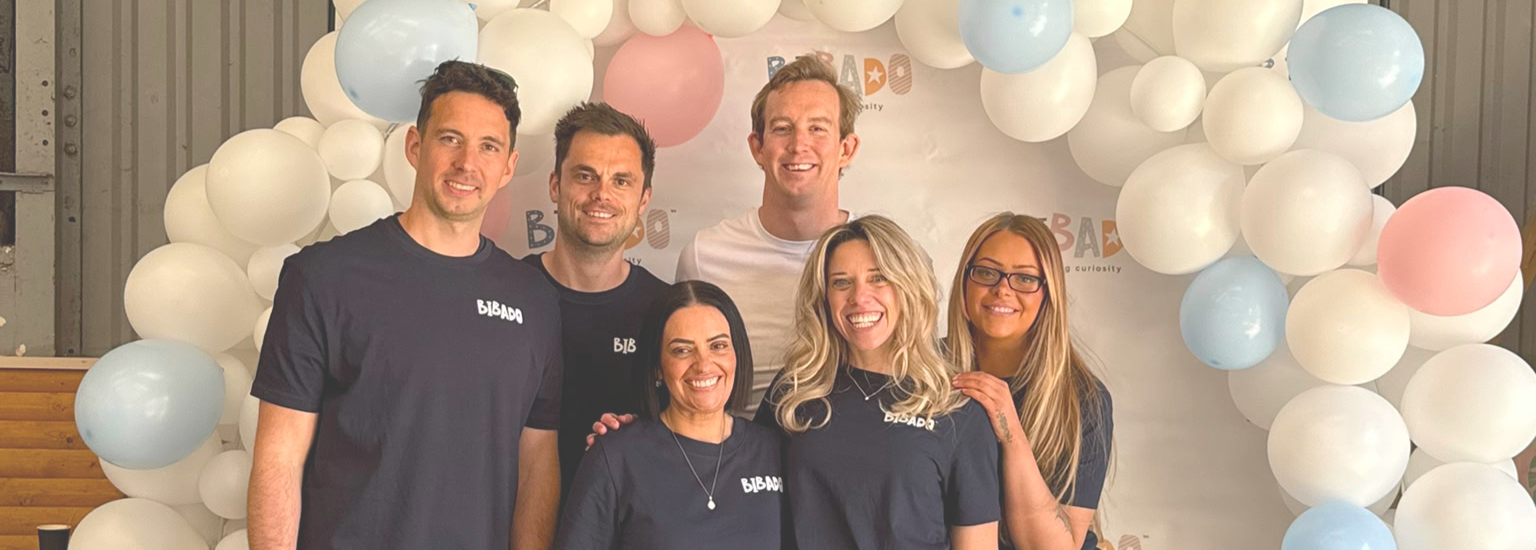 Group of people posing in front of a balloon arch with a visible Bibado brand logo.