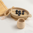Beige silicone suction bowl with oatmeal and blueberries, matching cup and spoon.