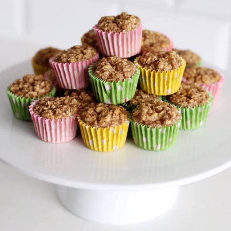 A stack of mini porridge bakes in pink, yellow, and green cupcake cases on a white cake stand.