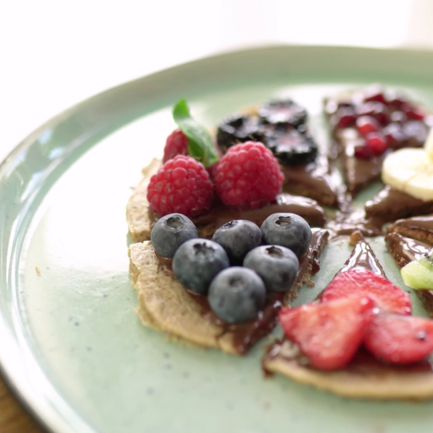 Sweet pancake pizza slices with chocolate spread and various fresh fruits on a light green plate.