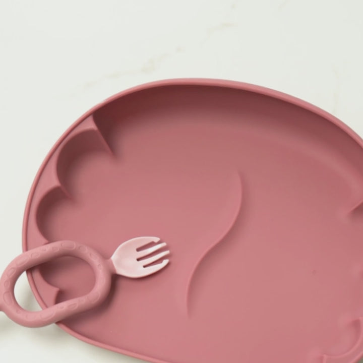 A beige silicone baby feeding plate with scalloped edges, shown on a white high chair. The tray contains white rice, curry, and a small matching silicone spoon. - Product image