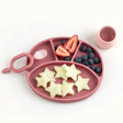 Pink /blush silicone plate with compartments filled with star-shaped fruit on a white background